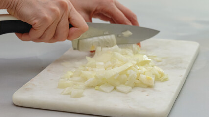 Obraz na płótnie Canvas Chopped white onion close up on marble cutting board. Woman hands with knife on background. Step by step cooking process