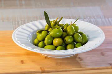 view of a plate of delicious looking olives on a wooden board on an out of focus background.