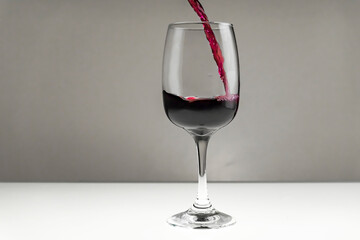 Red wine is poured from a bottle into a glass on a blurred background, close-up. Horizontal photo