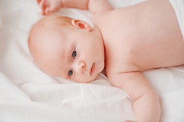 cute red-haired baby lies on a white bed. concept of baby care