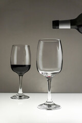 Red wine is poured from a bottle into a glass on a blurred background, close-up.Vertical photo
