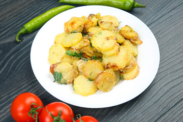 cooked fried potatoes with herbs and vegetables in a plate on a wooden table