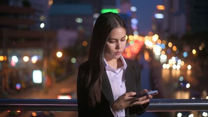 A young beautiful business woman is using smart phone in city over traffic lights at evening. business and technology concept..