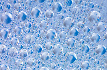 Water drops on blue glass as an abstract background.
