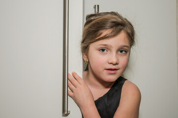 Little adorable girl child peeking out of the cabinet doors	
