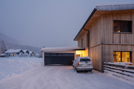 freshly snow cleared entrance in the dead of winter with a car in front of wooden house garage in the evening