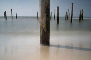 Focus on fLong exposure seascape. Taken at the North Sea in Petten with the pole village in the sea, Blue sky, sun and shodows. Focus on foreground