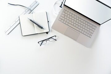 Silver gray laptop with empty screen, notebook, pen and glasses on a white office desk, copy space, high angle view from above
