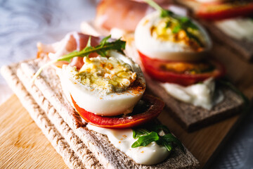crispbreads with smoked ham, tomatoes and eggs on a cutting board