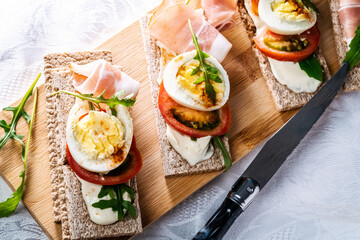 crispbreads with smoked ham, tomatoes and eggs on a cutting board