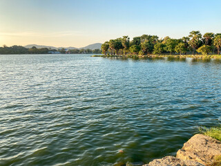 Morning lake in running park with green trees and small wind making wave on lake surface, the water look blue-green