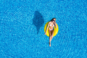 Aerial view of young brunette woman swimming on the inflatable big donut in the transparent turquoise sea. Top view of slim lady relaxing on her holidays