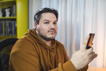 Selective focus shot of a moody cool guy with piercings sitting in a room using his phone