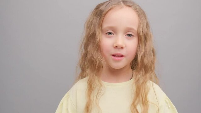 Little girl is surprised looking into the camera. Picture taken in the studio on a gray background. Super slow motion.