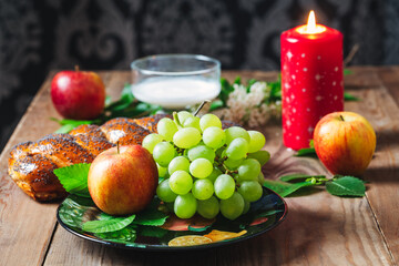 Wicker bun, apples, green grapes, wheat and a glass with milk on a wooden table. Jewish holiday Shavuot.