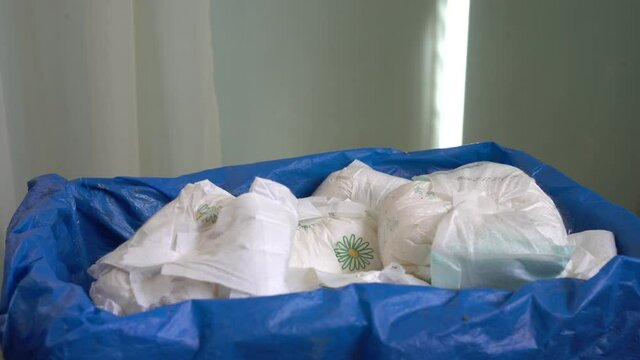 Mother is throwing away dirty diapers wetdiapers in waste bin. Pollution of the environment by plastic garbage. Disposable personal care products