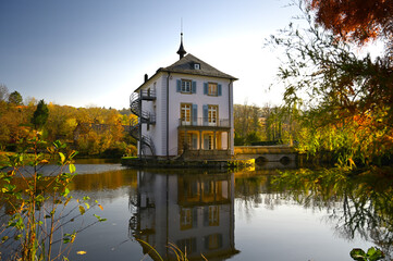 Fototapeta na wymiar A baroque house, called Trappenseeschlösschen, surrounded by Lake Trappensee in Heilbronn, Germany during autumn. The house and the colorful trees reflect in the water.