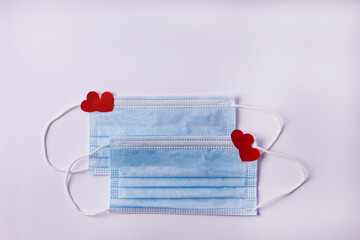 Two medical protective masks decorated with red hearts on a white background. Valentine's Day, love, medicine, covid 19 concept. Flat lay, copy space. 