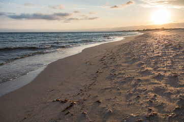 sandy beach by the sea on the background of the setting sun, soft evening light, horizontal photo