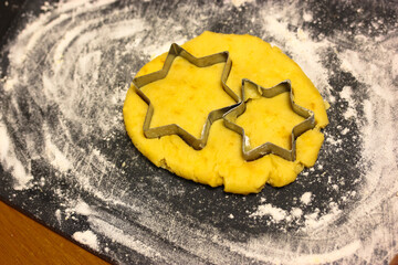 Star-shaped cookie cutter molds and freshly kneaded yellow dough inside, black cutting board...