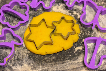 Star-shaped cookie cutter molds and freshly kneaded yellow dough inside, black cutting board...