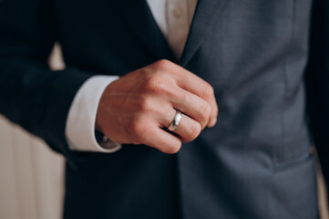 Obraz premium the groom in a black jacket and white shirt with a ring on his hand holds a jacket