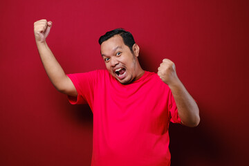 Fototapeta premium Young asian man happy and excited expressing winning gesture. Successful and celebrating over red background