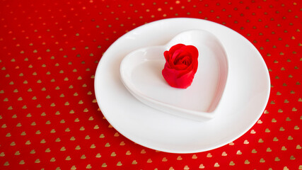 Place setting in red and white - for Valentine or other event. White plate in the shape of a heart with a decor of roses on a red background