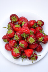 Strawberries on white plate. Freshly picked strawberry. Organic berries on white background. Village garden harvest.