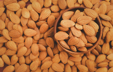 Almonds in brown wooden bowl on Background of big raw peeled almonds.Healthy food Concept.