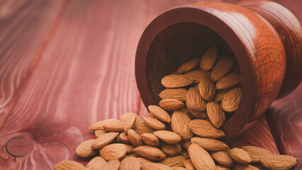 Almonds pour from brown wooden bowl on wooden table background.Healthy food Concept.