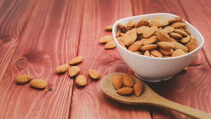 Almonds pour from wood spoon with white porcelain bowl on wooden table background.Healthy food Concept.