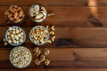 Organic mixed nuts in bowl on wooden table. Top view, Space for text. Walnut, Brazilian and pine nuts, almonds, hazelnuts and cashews