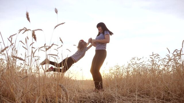 mom play with her daughter the park in wheat field. happy family people in the park concept. mom play is spinning daughter fun holding hands in wheat field. dream childhood happy family