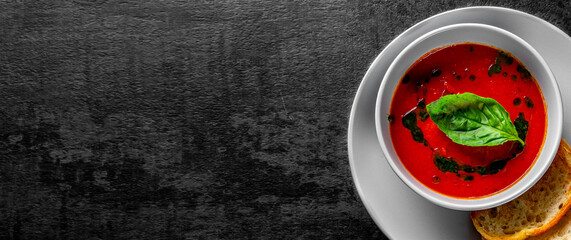 tomato soup with basil in a bowl on Dark grey black slate background