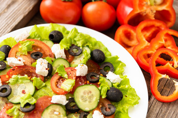 On the wooden table is a plate of Greek salad and feta cheese.