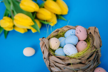 Happy Easter. Easter holiday decorations on trendy colored classic blue background. Creative spring composition with Easter elements - flowers and eggs in basket. Celebrating Easter concept at spring.