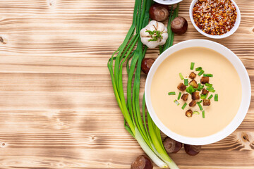 Delicious chestnut soup on a wooden background with seasonings and onions. Top view. Space to copy.