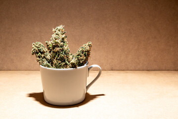 Ready to consume medical marihuana buds inside a coffee cup. Selective focus on brown background.
