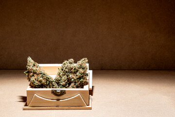 Details of some medical marihuana buds ready for consumption inside a wooden box. Selective focus on brown background.