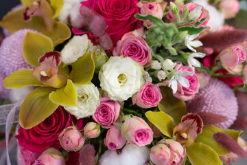 Floral arrangement with orchids, cotton and other flowers in a large hat box on a dark background.
