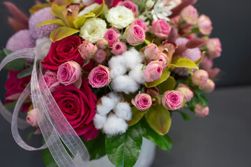 Floral arrangement with orchids, cotton and other flowers in a large hat box on a dark background.