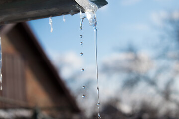 Icicle with water drops on a background of blue sky. View from the window