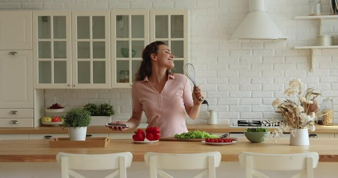 Housewife dance in kitchen listen playlist music on smartphone sing song use beater like microphone feels carefree enjoy food preparation at home. Hobby, cookery, weekend free time activity concept