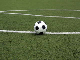 Classic ball for playing soccer in white with black accents lays on green synthetic grass  on the marking line near centre of sport playground