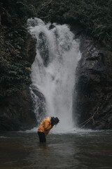An asian male traveler enjoying the beauty of rainforest waterfall.A male explorer in the waterfall pool.Camping and hiking lifestyle.Into the wild.