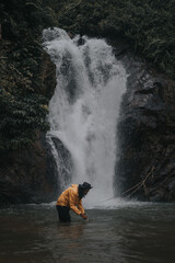 An asian male traveler enjoying the beauty of rainforest waterfall.A male explorer in the waterfall pool.Camping and hiking lifestyle.Into the wild.