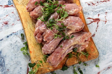 Raw Chicken neck decorated with green sprouts on a kitchen wooden board on a light marble background