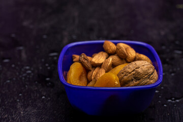 A bowl full of almonds walnut and apricots with back background.