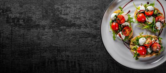 Italian bruschetta with roasted tomatoes, mozzarella cheese, balsamic vinegar and herbs on plate on...